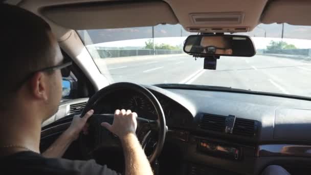 サングラスをかけた若者がハンドルを握って車を運転している 白人の男は夏の日に高速道路で車に乗っている スローモーションを閉じる ビュー — ストック動画