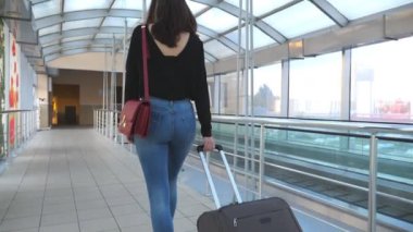 Yüksek topuklu ayakkabılı, tekerlekli bavulu yuvarlayan tanınmamış bir kız. İş kadınının bacakları bavuluyla terminal koridorundan geçiyor. Bayan seyahate çıkıyor. Seyahat konsepti. Yavaş çekim. Yakın çekim..