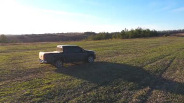 Yaz günü çayırda uçan kamyonet görüntüsü. Hasattan sonra siyah araba tarladan geçiyor. Çiftlik arazisine doğru giden off-road aracının üzerinden uçuyor. Arka planda güzel güneş ışığı.