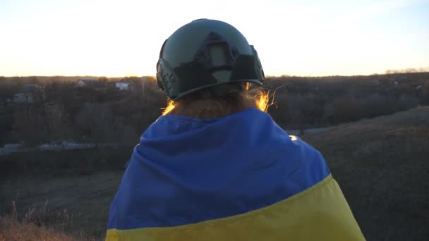 举着乌克兰国旗的不明身份的乌克兰陆军士兵看着日落 身着军服头戴头盔的女孩凝视着地平线 等待战胜俄国侵略的胜利 抵抗入侵 — 图库视频影像