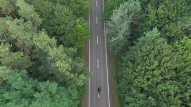 Motorcyclist racing his motorcycle on country road at green wood. Aerial shot to biker riding on motorbike through forest road. Man drive bike during trip. Concept of freedom and adventure. Top view.