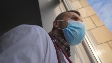 Pensive doctor at medical uniform look of out window. Overworked and sad medic in protective mask after hard day at work. Tired physician during COVID-19 pandemic. Healthcare concept. Bottom view.