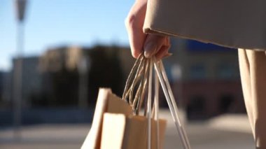 Hands of young woman carry shopping bags walking along urban street. Female arms hold paper packages going on city square after purchases. Concept of sales and discounts. Slow motion Close up.