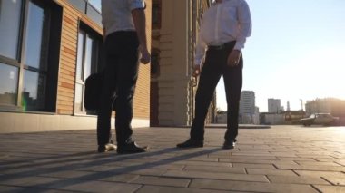 Successful manager passing a black briefcase to his partner near office building during business meeting. Young male coworkers shaking hands and leaving in different directions. Dolly shot Slow motion