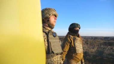 Ukrainian army soldiers stands outdoor at sunset time and waves flag of Ukraine. People in military uniform lifted up flag against blue sky. Victory at war. Resistance to russian invasion. Slow motion