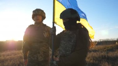 Soldiers of ukrainian army walks at field with flag of Ukraine. People in military uniform waving national yellow-blue flag as sign of victory against russian aggression. Invasion resistance concept.