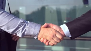 Ofis binasının yakınında birbirini selamlayan başarılı iş adamlarına yakın durun. İki genç meslektaşın şehir ortamında buluşup el sıkışıyor. İş ortaklarının el sıkışması. Yan görünüm.