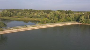 Bisikletçi, yaz günü nehir köprüsünden motosikletle geçiyor. Adam Lake Road 'da modern spor motosikletine hızlı biniyor. Motosikletli baraj yolunda bisikletiyle yarışıyor. Macera kavramı. Hava görüntüsü.