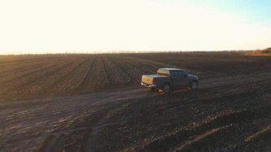 Aerial shot of pickup truck driving through plowed field after harvesting. Flying over car moving among farmland at autumn. Off road vehicle riding along ploughed meadow. Concept of agronomy farming.