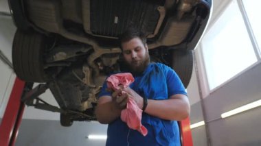 Garajda sıkı çalıştıktan sonra, genç sakallı bir tamirci ellerini yakıt yağından bir bezle siliyor. Gülümseyen oto tamircisinin portresi kaldırılmış arabanın arka planında duran kameraya bakar. Yavaş çekim.