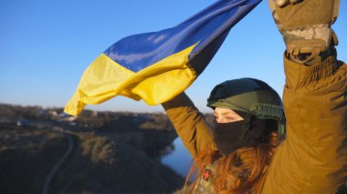 Ukrayna bayrağı sallayan Ukrayna ordusunun kadın askeri. Askeri üniformalı ve kasklı kız sarı-mavi bayrak kaldırdı. Rus saldırısına karşı zafer. İstila direnci konsepti. Yavaşla.