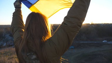 Ukrayna bayrağını çekmek için tepenin zirvesine koşan Ukraynalı kadın asker. Askeri üniformalı bir kadın Rus saldırısına karşı zafer sembolü olarak bayrak sallıyor. Savaş konsepti bitti..