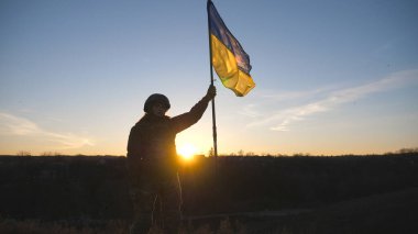 Askeri üniformalı kadın gün batımına karşı duruyor ve Ukrayna bayrağını kaldırıyor. Bayrak sallayan Ukraynalı kadın asker. Rus saldırısına karşı zafer. İstila direnişi kavramı.