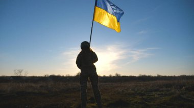 Soldier of ukrainian army holding waving flag of Ukraine. Woman in military uniform and helmet lifted up yellow-blue flag. Victory against russian aggression. Invasion resistance concept. Slow motion.