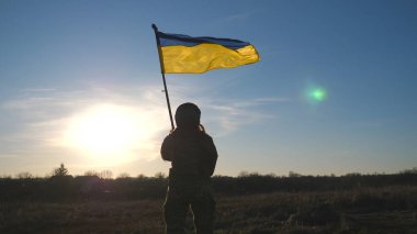 Ukrayna bayrağı sallayan Ukraynalı kadın Ukraynalı asker. Askeri üniformalı ve kasklı bir kadın mavi gökyüzüne bayrak kaldırdı. Rus saldırısına karşı zafer. İstila direnişi kavramı