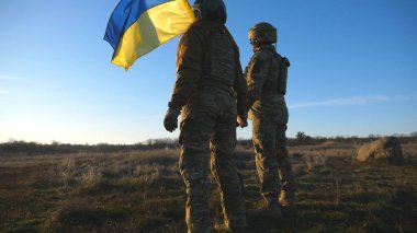 Ukrayna bayrağını çekmek için tepenin zirvesine koşan Ukrayna ordusunun askerleri. Askeri üniformalı insanlar Rus saldırısına karşı zafer sembolü olarak bayrak sallıyor. Savaş konsepti bitti..