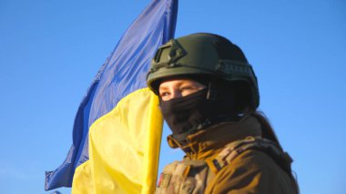 Ukrayna bayrağı sallayan Ukraynalı kadın Ukraynalı asker. Askeri üniformalı ve kasklı bir kadın mavi gökyüzüne bayrak kaldırdı. Rus saldırısına karşı zafer. İstila direnişi kavramı
