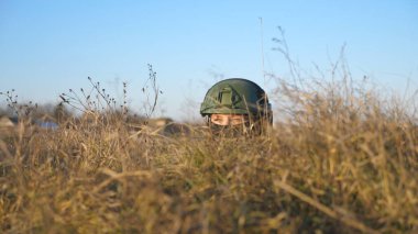 Military medic in outfit and helmet hiding in a trench during shelling and leaves after the enemy attack. Ukrainian female soldier hides behind a hill and looking from the shelter. War in Ukraine.