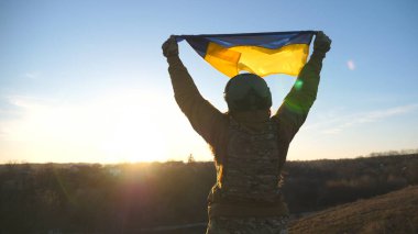 Ukrayna ordusunun kadın askeri Ukrayna bayrağını dalgalandırmak için tepeye koşuyor. Askeri üniformalı kadın, Rus saldırısına karşı zafer işareti olarak gün batımına karşı bayrak kaldırdı. Yavaş çekim.