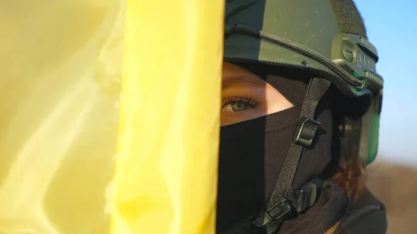 Female ukrainian army soldier holding waving flag of Ukraine. Woman in military uniform and helmet lifted up flag against blue sky. Victory against Russian aggression. Invasion resistance concept