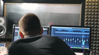 Rear back view of unrecognizable young male sound engineer and music producer working in the modern recording studio. Audio editor creation a new song on personal computer. Close up Slow motion.