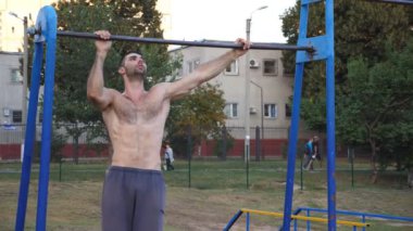 Genç atlet spor sahasında yatay barda yoğun egzersizler yapıyor. Spor yaparken barfiks çeken güçlü bir jimnastikçi. Açık havada kaslı üstsüz sporcu eğitimi. Sportif yaşam tarzı kavramı.