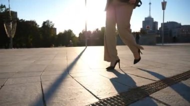 Kendine güvenen bir iş kadını işe gidip geliyor. Güneş gözlüklü güzel bayan yüksek topuklu ayakkabılarla kaldırımda yürüyor. Çekici esmer kız arka planda güneş ışığıyla şehir caddesinde dolaşıyor. Yavaş çekim.
