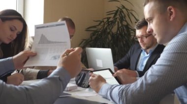 Modern ofiste masada oturan ve yeni bir proje üzerinde çalışan bir grup genç iş adamı. Meslektaşlar çalışırken belgeleri dikkatle incelerler. Ofis çalışanları iş geliştirmekle meşgul. Yavaş çekim.