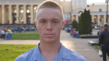 Portrait of young serious businessman in shirt looking into camera at cityscape background. Close up of successful man standing at city environment. Face of confident guy. Front view Slow motion.
