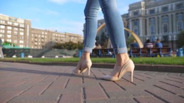 Female legs in high heels shoes walking in urban street. Feet of young woman in high-heeled footwear going in city. Girl stepping on sidewalk. Rear back view Slow motion Close up.
