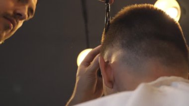 Male barber combing and cutting hair of customer by hairbrush and scissors in barbershop. Hands of hairdresser trimming hair of his client in salon. Hairstyling process. Low angle view Slow motion.