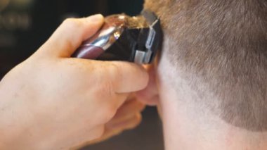 Arms of hairdresser making male haircut to customer with clipper in salon. Hands of hairstylist cutting hair of guy with electric razor in trendy barbershop. Barber shaving man with trimmer. Rear view