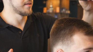 Close up of professional male hairstylist combing hair of his customer in trendy barbershop. Young guy getting his hair dressed at salon. Hairstyling process. Side view Slow motion.