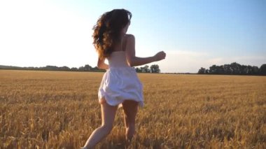 Unrecognizable girl beautiful is run and arms up, along the field under blue sky at sunset. Back view. Slow motion