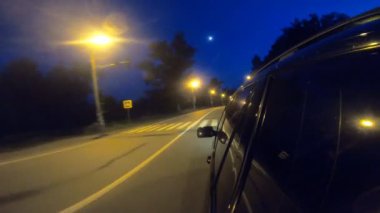Siyah SUV gece şehir otobanından geçiyor. Akşamları otomobille şehir sokaklarında dolaşmak. Araç otoyol boyunca hızla ilerliyor. Kentsel alanlarda trafik var. Yolculuk mu seyahat konsepti mi? Bakış açısı.