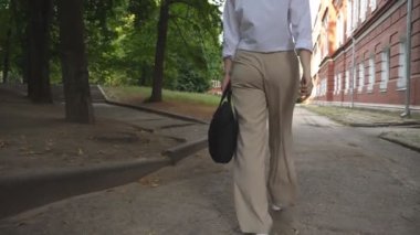 Attractive business woman in formal wear going to work through city park. Elegant girl with briefcase on her way at office. Success or career concept. Businesswoman commute to job. Slow motion.
