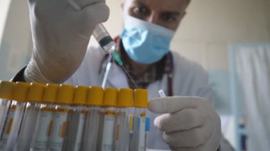 Bilim adamı ya da doktor şırınga kullanarak test tüplerini sıvıyla dolduruyor. Tıbbi maske takan doktor ve eldivenler laboratuarda çalışıyor. Sıhhiye COVID-19 'un analizlerini kontrol ediyor. Sağlık sigortası konsepti. Kapat..