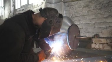 Kaynakçı, metal fabrikasında iki çelik detayı arasında bağlantı kuruyor. Endüstriyel üretimde koruyucu maske kaynak işçisi. Metal kaynak yapan adam. Yavaşça kapat..