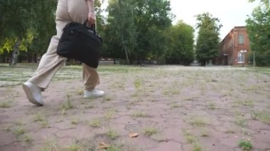 Legs of unrecognizable businesswoman going through urban park at summer day. Attractive girl in formal wear walking at city after work. Woman with bag stepping outdoor. Job concept. Slow motion.