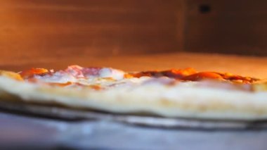 Erkek aşçı fırına kürekle pizza koyup mutfak restoranında kapatıyor. Genç aşçı mutfakta fırında lezzetli yemekler pişirecek. Pizzacıda yemek pişirme süreci. Kapat..