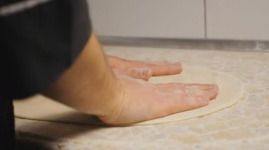 Aşçının erkek kollarını kapayarak mutfaktaki ahşap bir yüzeyde hamur işi oluşturuyorlar. Restorandaki mutfak masasında pizza için un hamuru şekillendiren şefin elleri. Yemek hazırlama kavramı. Yavaş çekim.