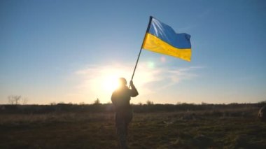 Female ukrainian army soldier walking to the peak of hill that to raise Ukraine flag. Woman in military uniform holding waving flag as symbol of victory against russian aggression. End of war concept.