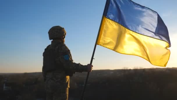 在日落时分举着乌克兰国旗的乌克兰士兵 身穿军服 头戴头盔的人升起了国旗 战胜俄国侵略的胜利抵抗入侵的概念 — 图库视频影像