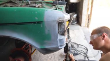 Tamirci garajda elektrikli aletle araba parlatan koruyucu gözlük takıyor. Otomobili tamir etmekte ustaymış. Kıyma makinesi kullanarak eski arabanın gövdesini öğüten adam. Aracın bakımını yapan adam..