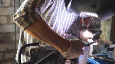 Garajdaki kaynakçı metal parçalarının işlemlerini kapat. Tamirci ya da kaynakçı işi için kaynak makinesi kullanıyor ve flaşlara karşı koruyucu maske takıyor. Yavaş çekim Dolly..
