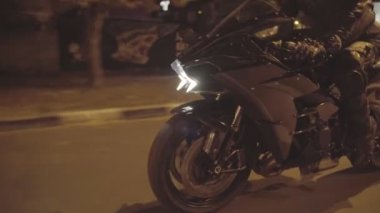 Koruyucu moto ekipmanlı erkek motorcu gece yolunda güçlü bir motosikletle hareket ediyor. Akşam caddesinde modern spor motosiklet kullanan motosikletli bir motosikletli. Özgürlük ve macera kavramı. Kapat..