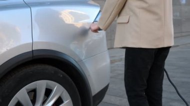 Kadın eli, priz kapağını açıp şarj aletini takıyor. Kadın, elektrikli aracının bataryalarını doldurmaya başlıyor. Sıfır emisyonlu çevre dostu otomatik