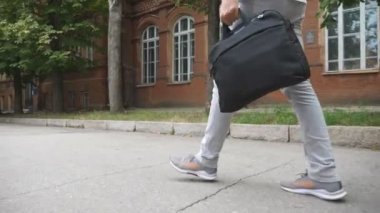 Şehir caddesinde yürüyen evrak çantalı tanınmayan iş adamının ya da öğrencinin bacaklarını kapatın. Ofise giderken günlük giysiler giyen kendine güvenen genç bir adam. Yavaş çekim.