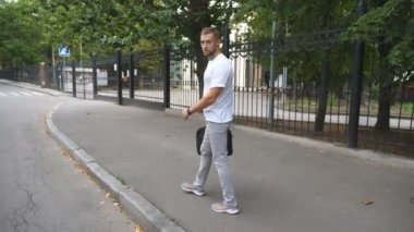 Şehir caddesinde dolaşan yakışıklı bir adam. Evrak çantalı genç işadamı kameraya bakıyor ve gülümsüyor. Dışarıda yürürken neşeli duygular gösteren mutlu bir adam. Yavaş çekim.