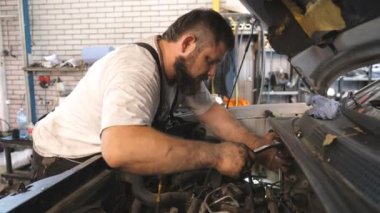 Tamirci atölyede ya da serviste anahtarı kullanarak arabanın motorunu tamir ediyor. Profesyonel oto tamircisi araç kaputu altında çalışır. Otomobil tamircisi garajda. Bakım ve tanı kavramı